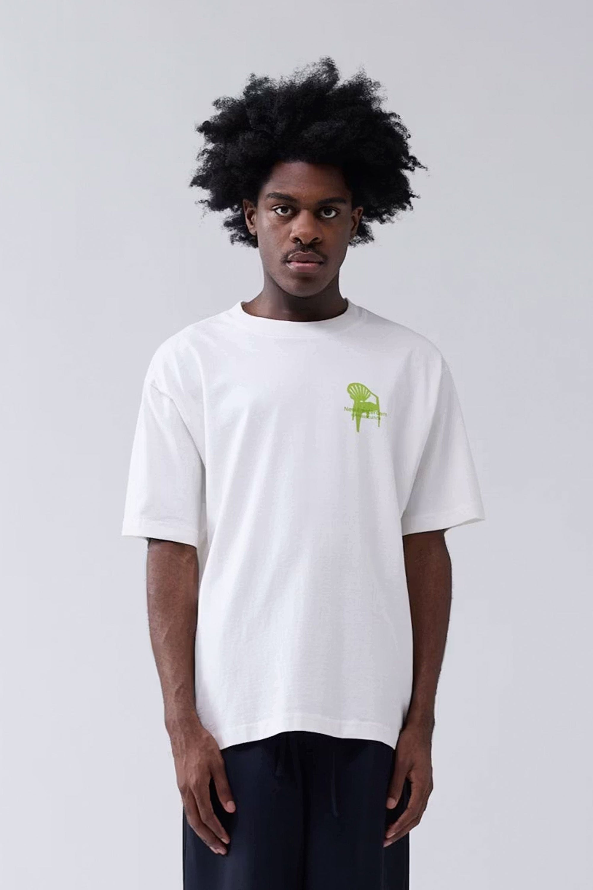 Person wearing a white t-shirt with a green logo on a plain background