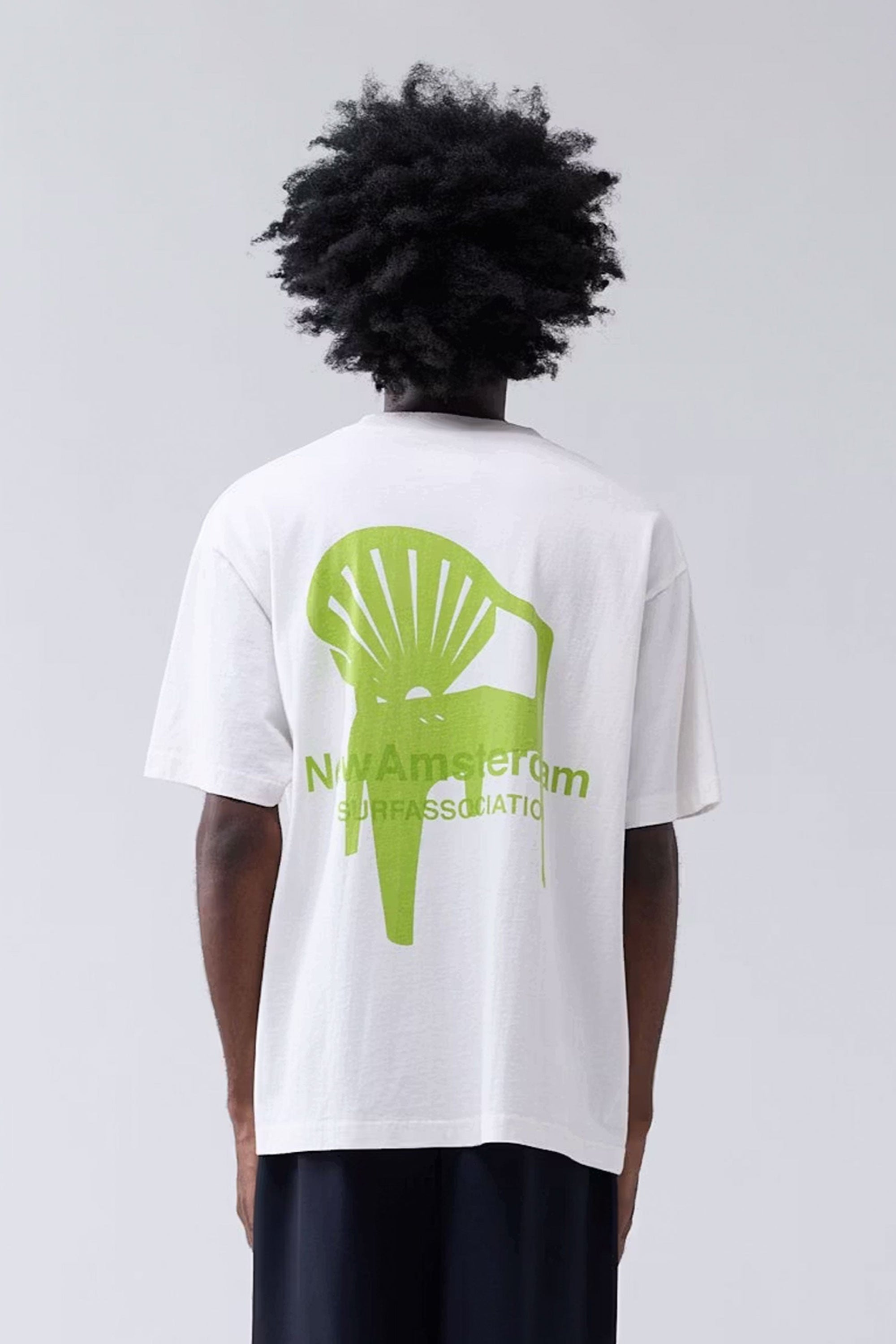 Person wearing a white t-shirt with a green graphic and text on the back, standing against a plain background.