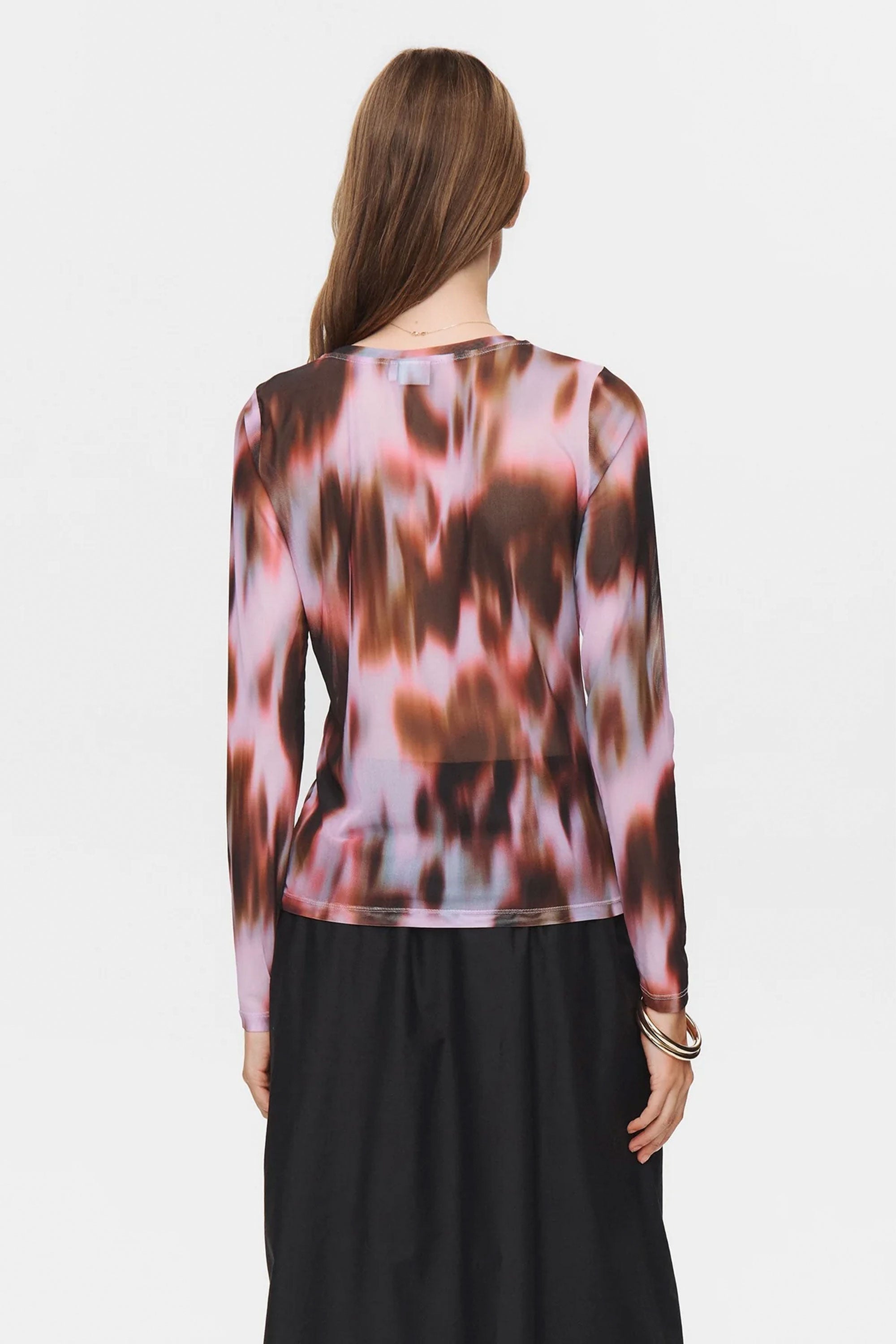 Woman wearing a long-sleeve, multicolored patterned top with a plain background