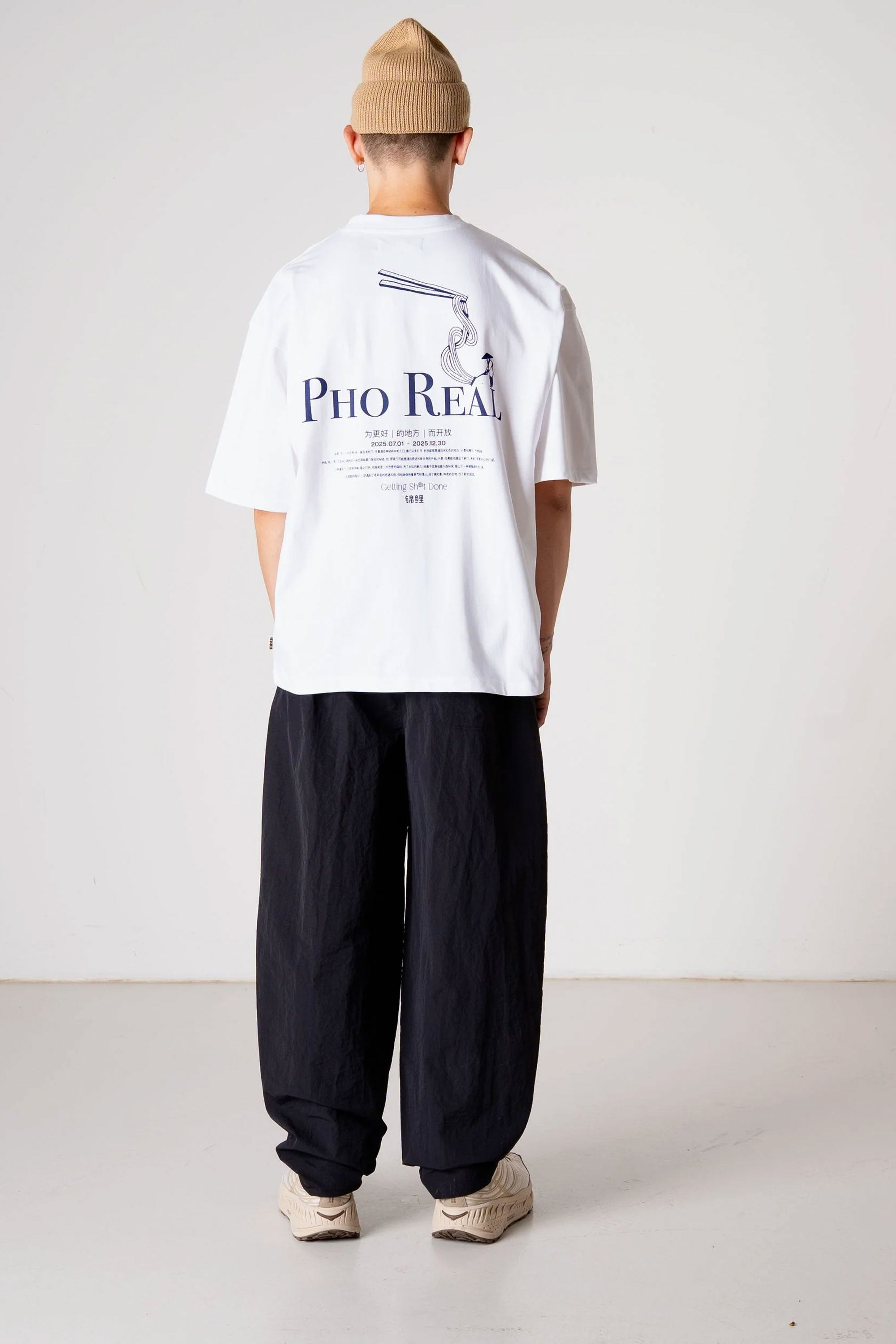 Person wearing a white t-shirt with text and black pants on a plain background